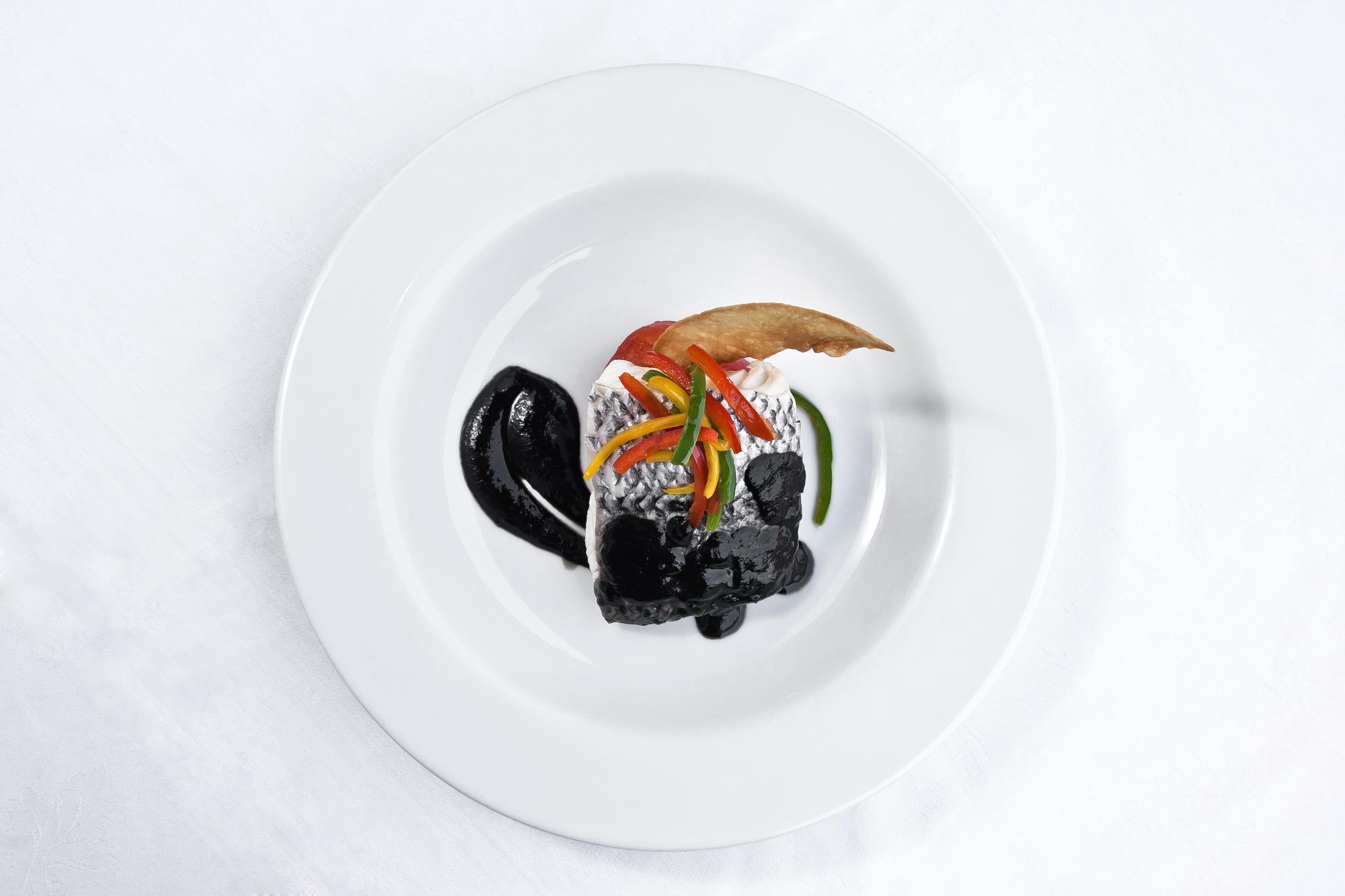 Finished signature dish on a dark plate with tech garnish